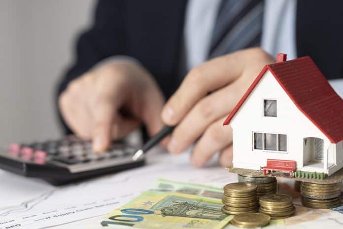 Une personne utilisant une calculatrice avec une maison miniature et des euros sur la table