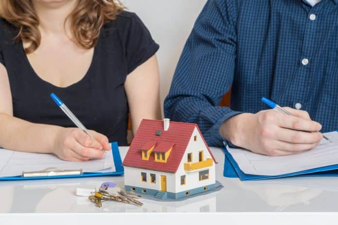 Un couple signant des documents avec une maison miniature et des clés sur la table