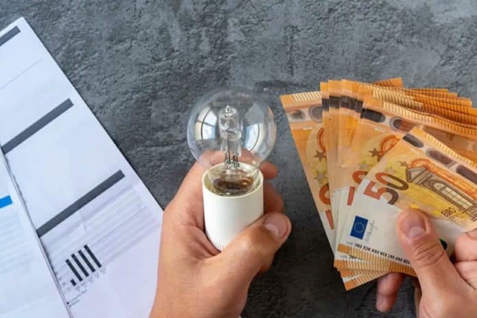 Des mains tenant une ampoule et des billets de cinquante euros à côté d'une facture d'électricité.