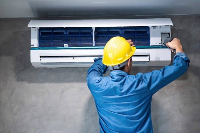 Technicien en casque jaune entretenant une unité de climatisation murale