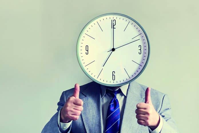 Un homme en costume avec une horloge à la place de la tête et faisant un geste de pouce en l'air.