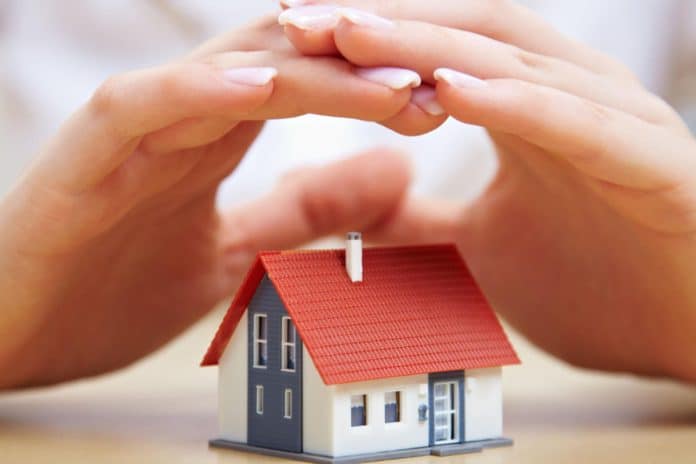 Mains protégeant une petite maison modèle pour illustrer la sécurité à la maison Mains protégeant une petite maison modèle pour illustrer la sécurité à la maison