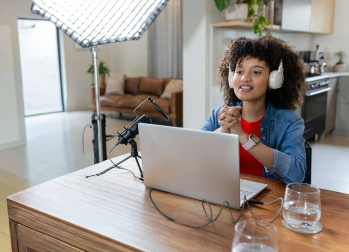African-American woman recording podcast with laptop, mic and headset at desk at home, copy space Jeune influenceur